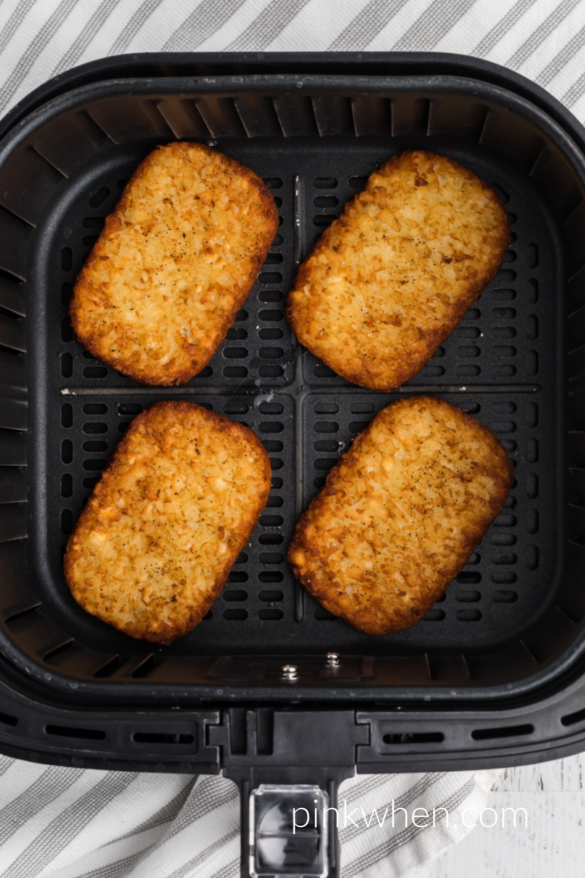 Crispy brown hash brown patties in the air fryer basket. 