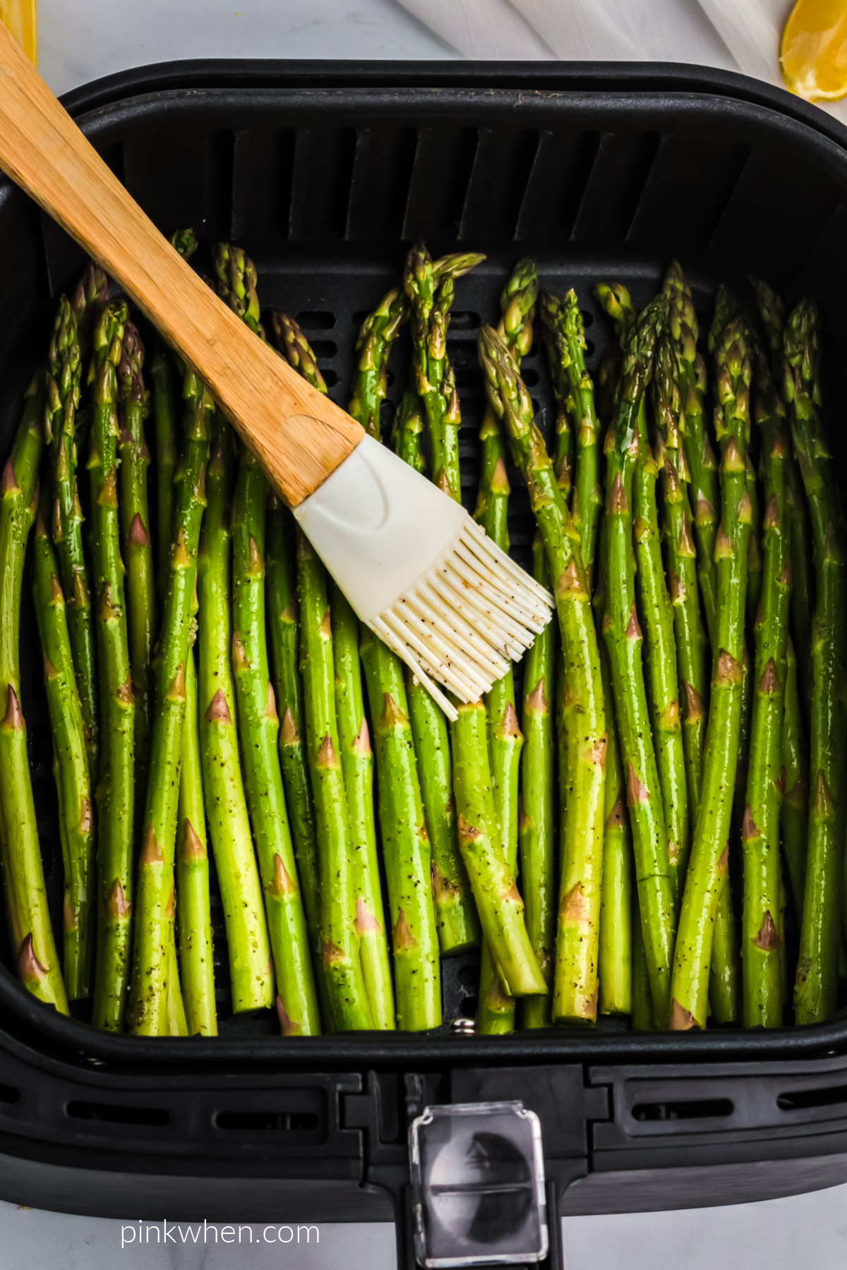 Asparagus in the air fryer basket being brushed with olive oil before air frying.