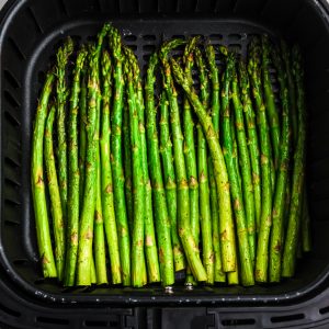 Air fried asparagus in the basket of the air fryer.