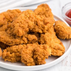 Chicken strips on a white plate that were frozen but cooked in the air fryer.
