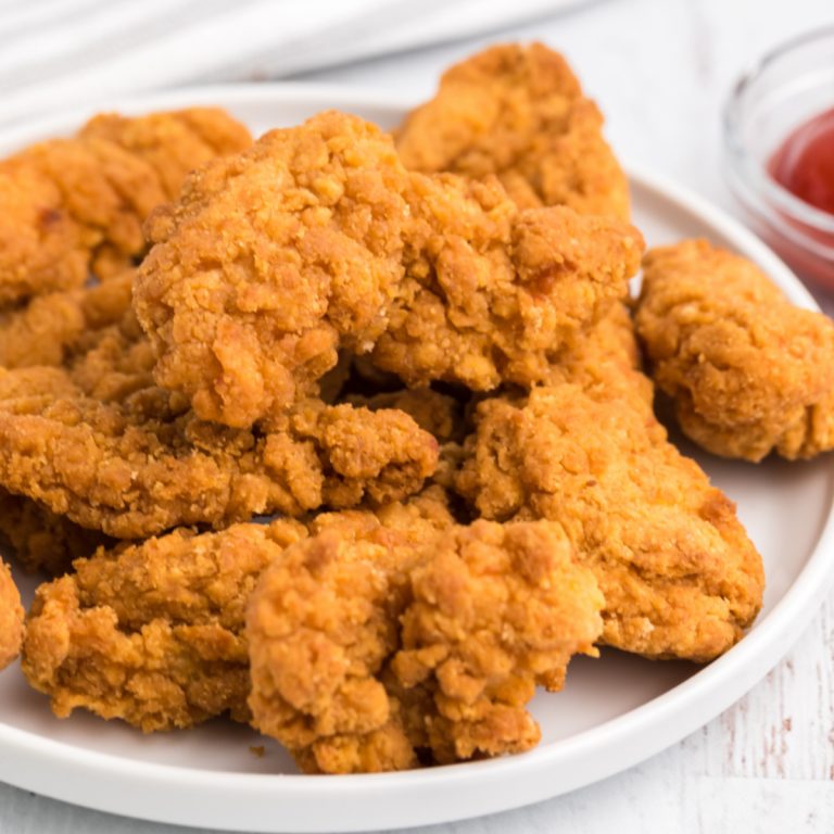 Chicken strips on a white plate that were frozen but cooked in the air fryer.
