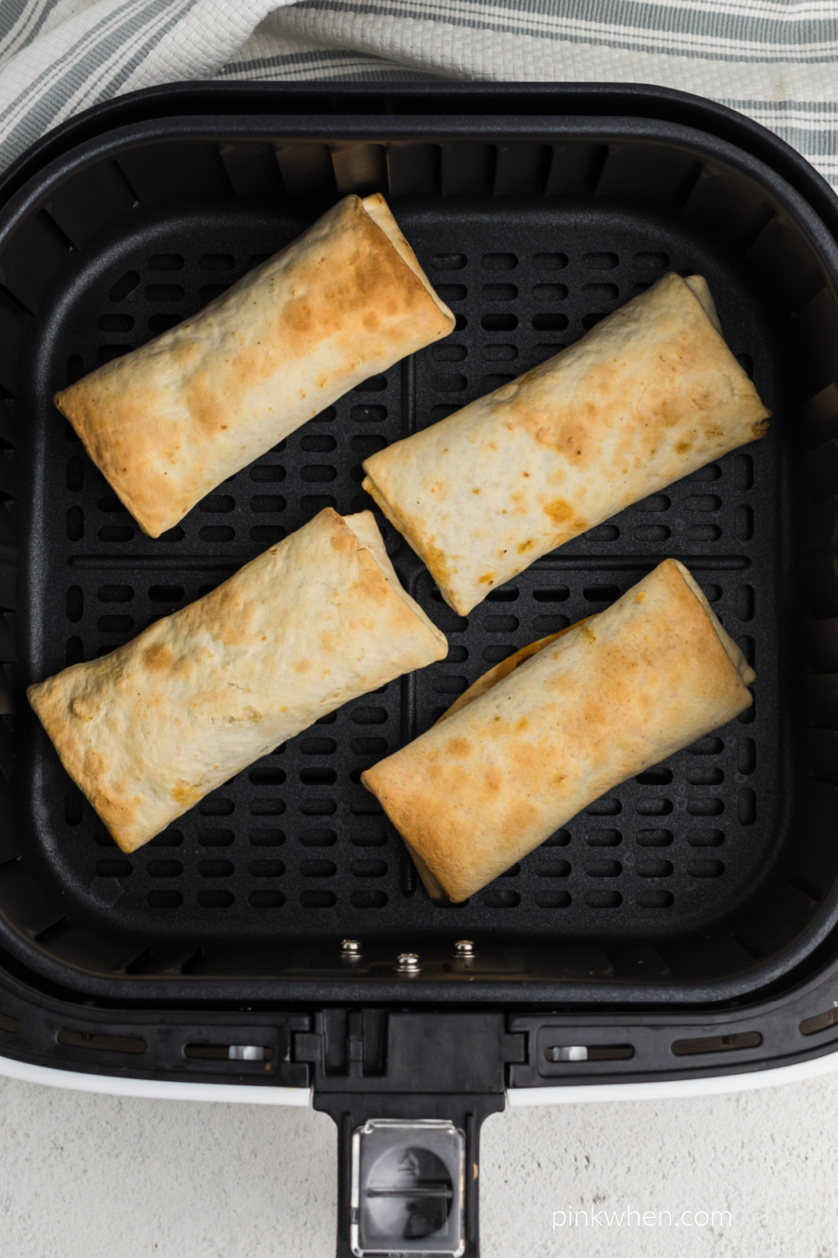Cooked frozen burritos in air fryer basket.