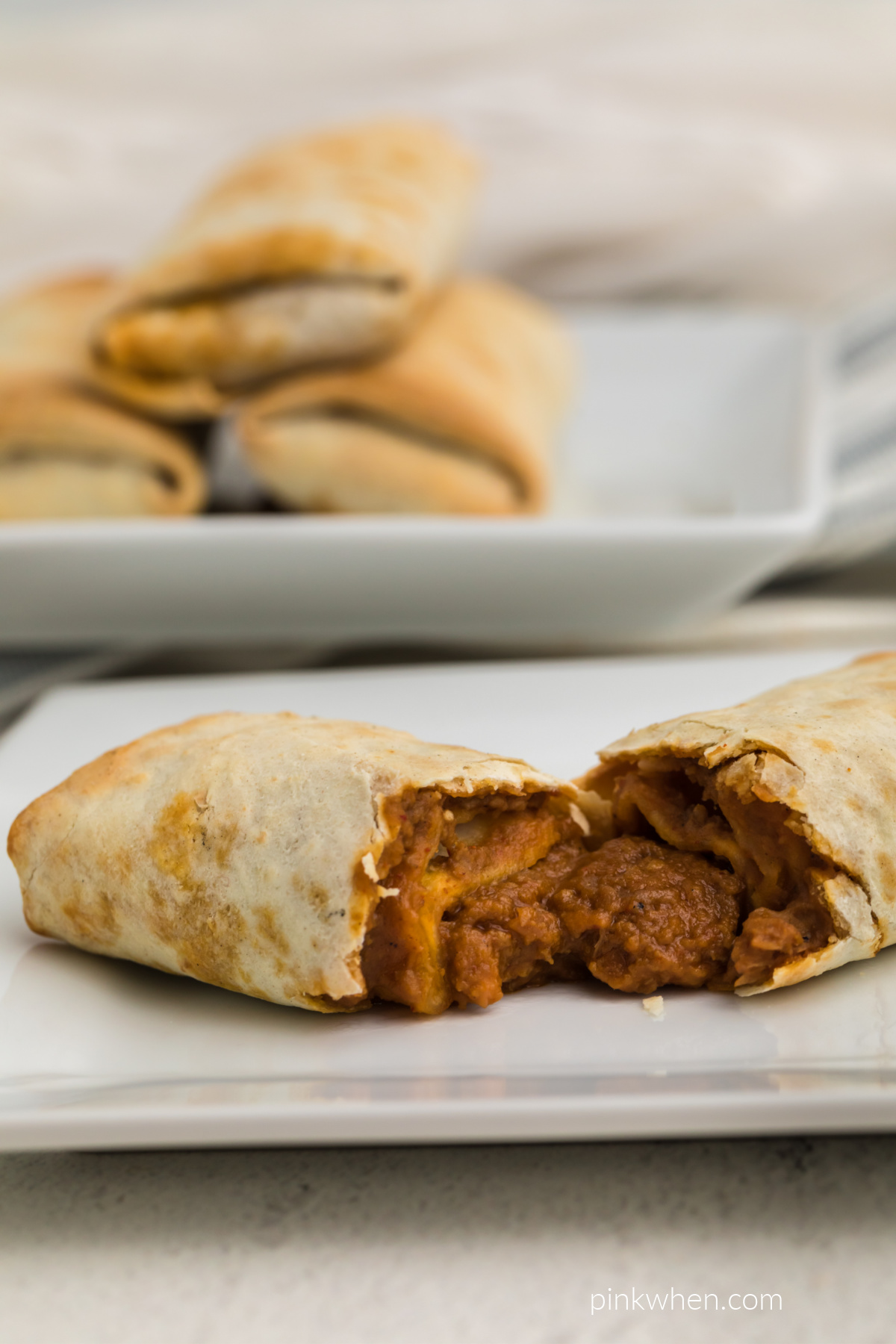Burritos stacked on a plate in the background and a burrito on a plate in the foreground ready to be eaten. 