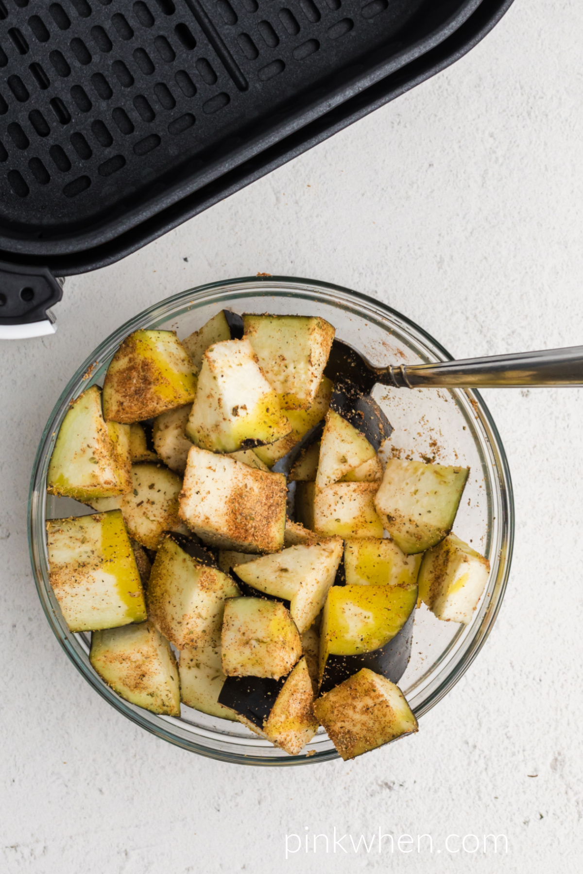 Eggplant pieces tossed in olive oil and seasonings in a bowl and ready to be placed into the prepared air fryer basket.