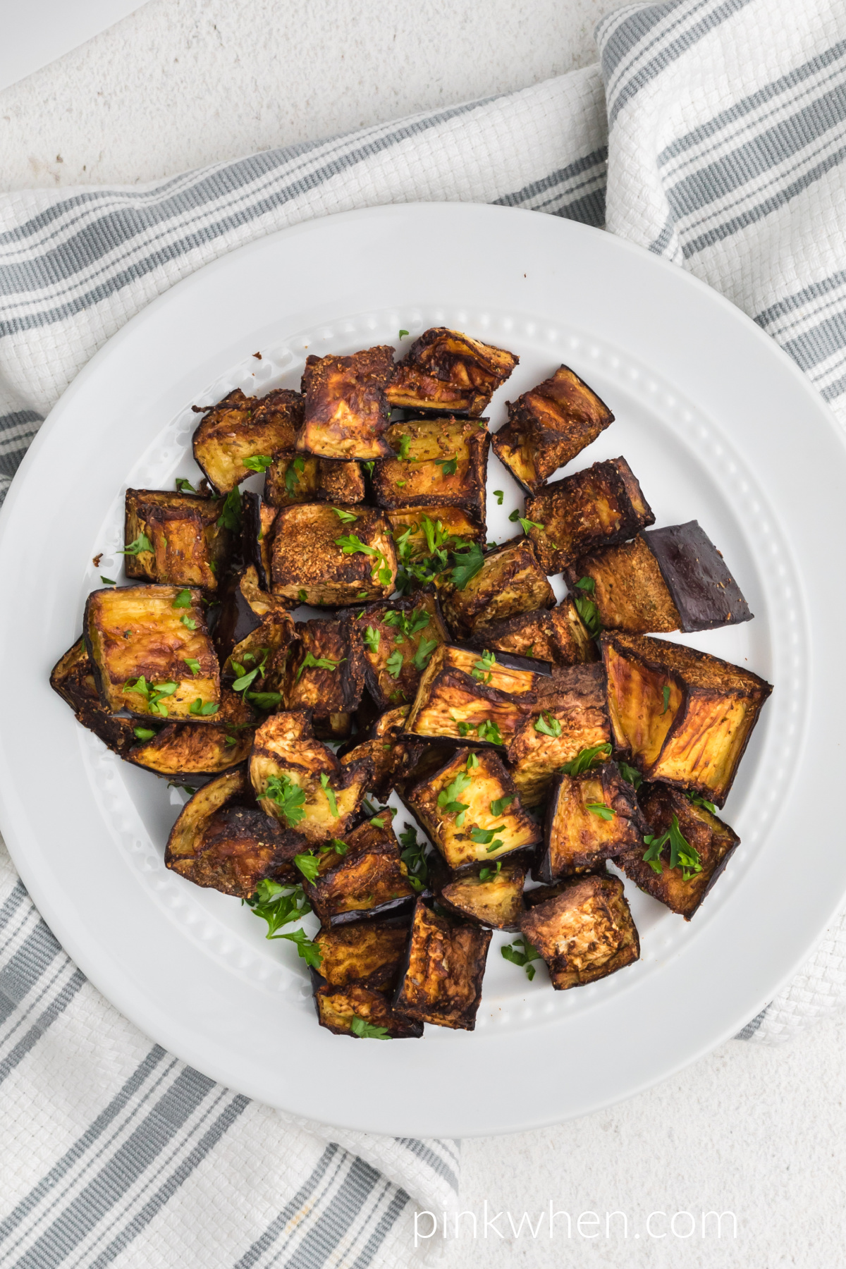 Over head shot of seasoned crispy air fryer eggplant in a white bowl.
