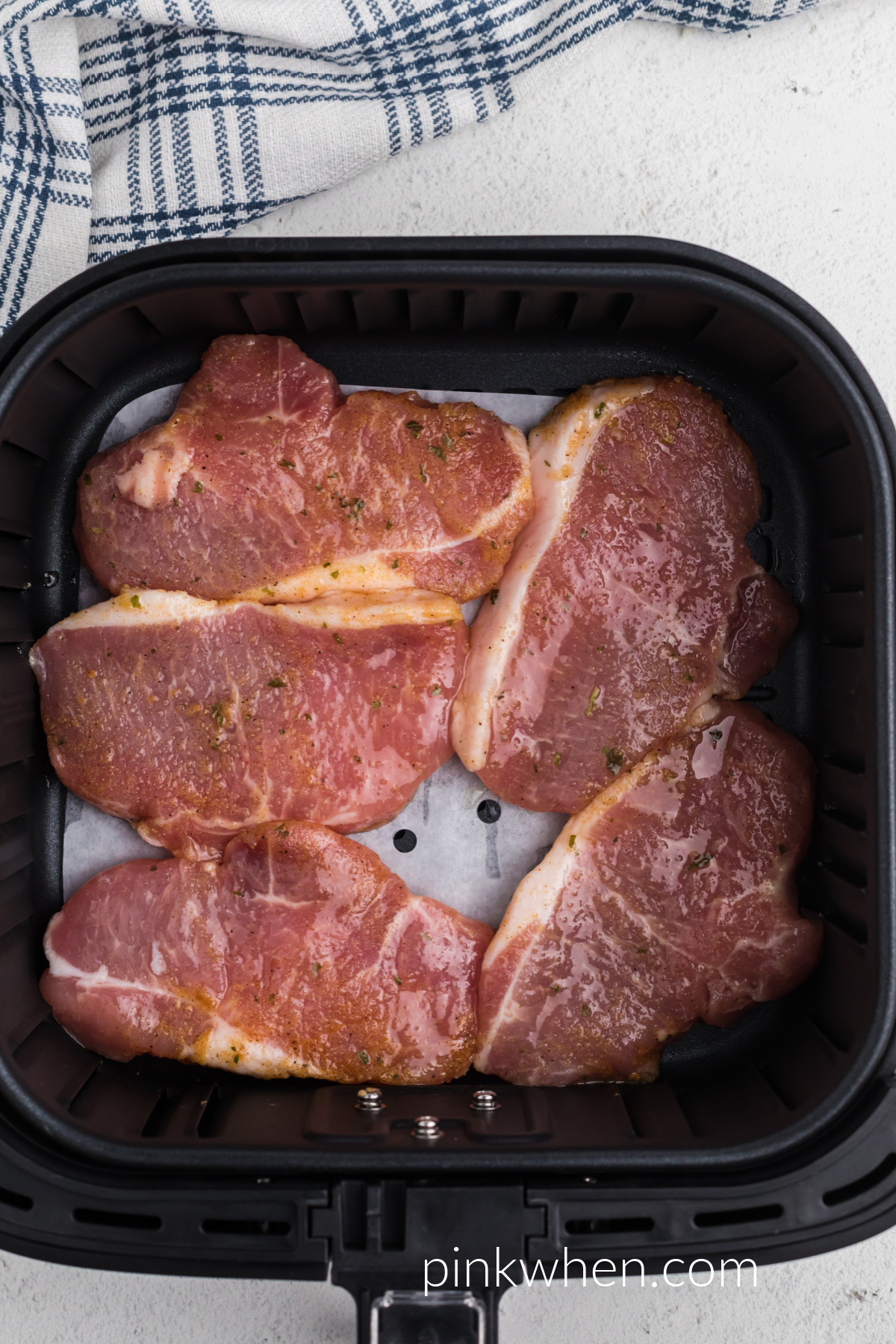 pork chops lined in a single layer in the air fryer basket on top of parchment paper. 