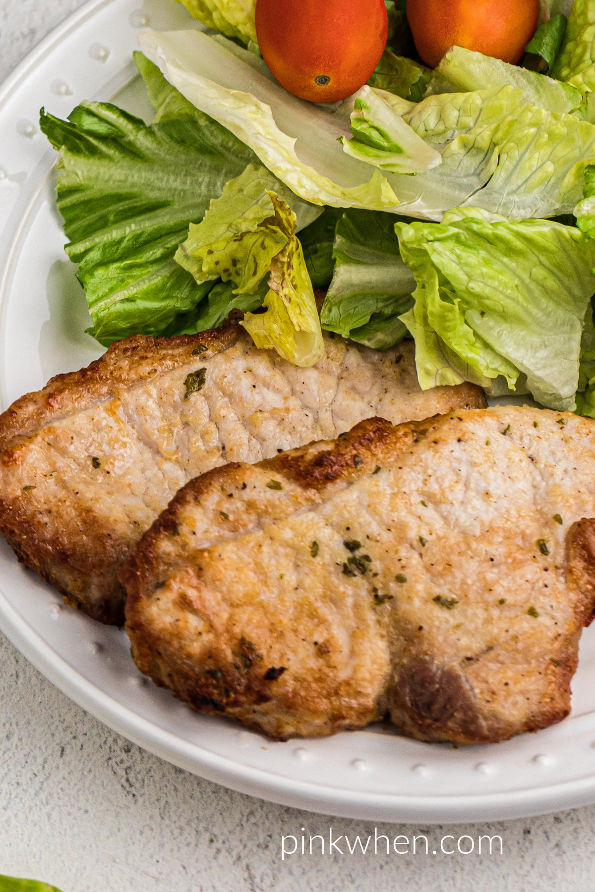 Seasoned air fryer pork chops with no breading on a white plate with a salad and ready to serve. 