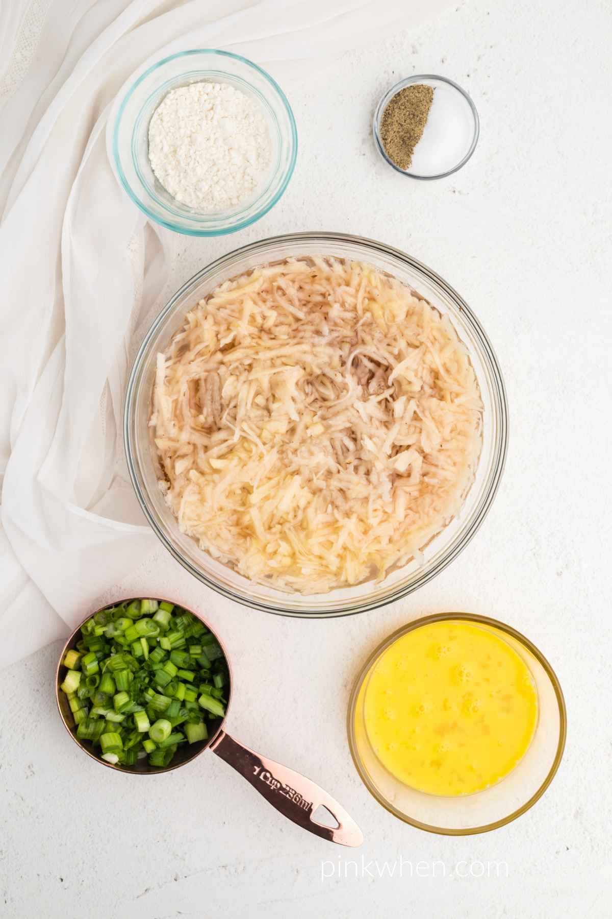 shredded potato soaking in water surrounded by other ingredients. 