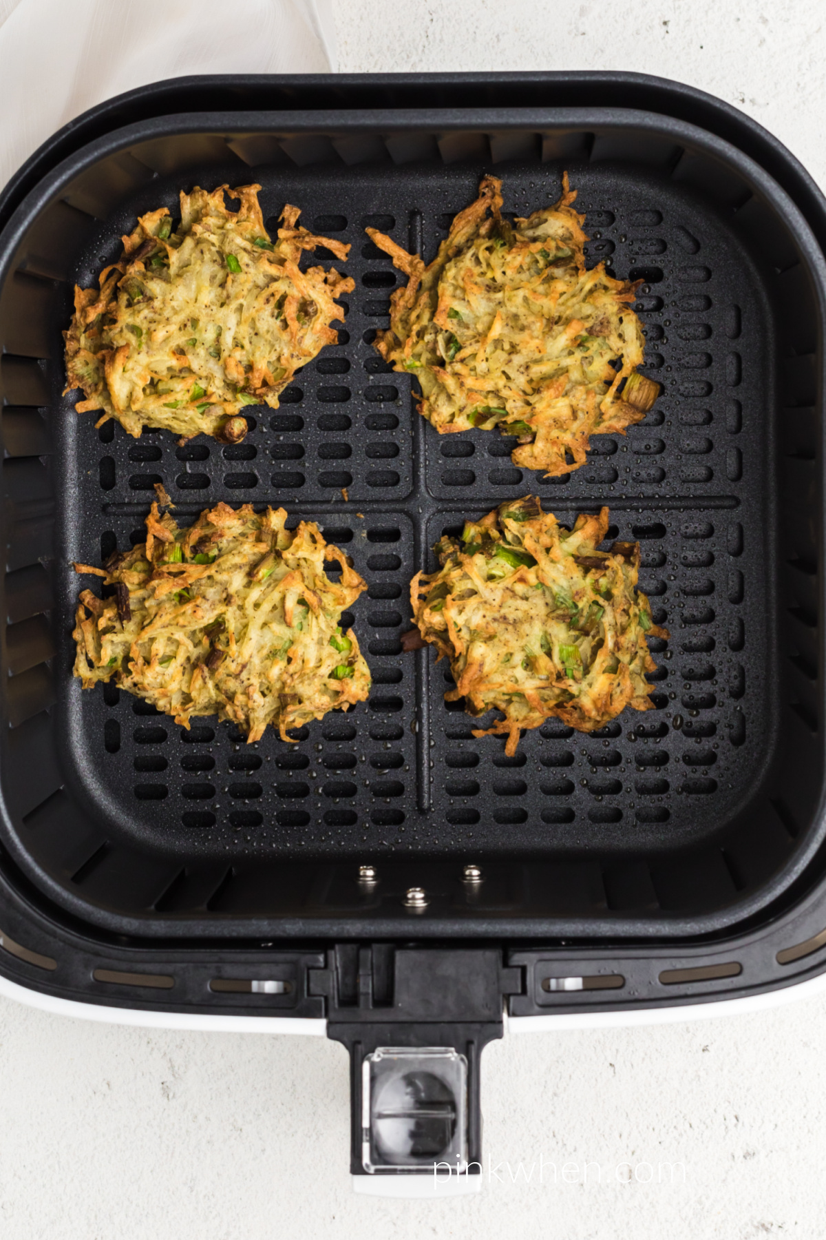 Golden brown air fried potato fritters in the basket of the air fryer. 