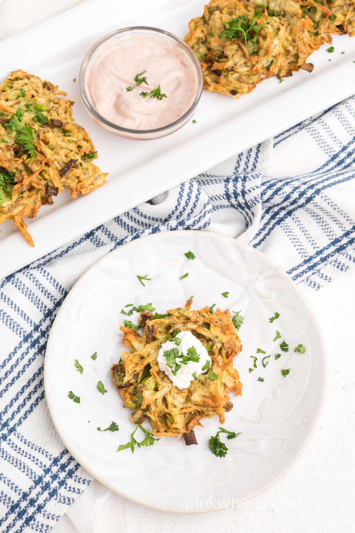Potato fritter on a white plate garnished with sour cream and fresh parsley. 