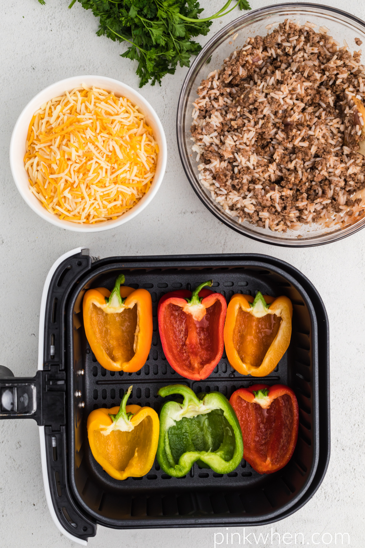 Peppers in the basket of the air fryer ready to be stuffed with mixture. 