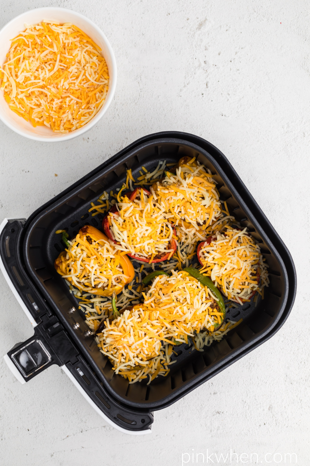 Air Fryer Stuffed Peppers topped with fresh shredded cheese and ready to be placed back into the air fryer. 