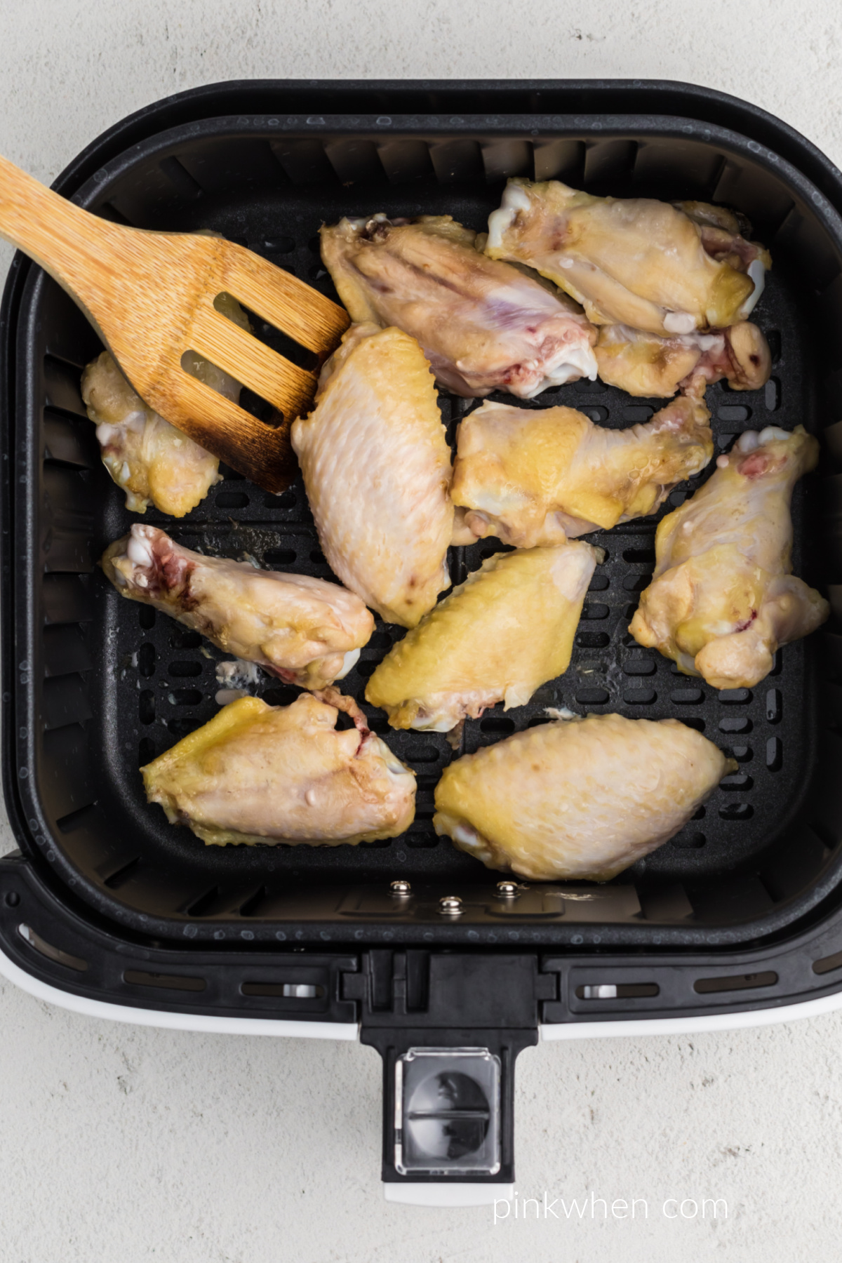 Naked wings semi thawed and half cooked in the basket of the air fryer. 