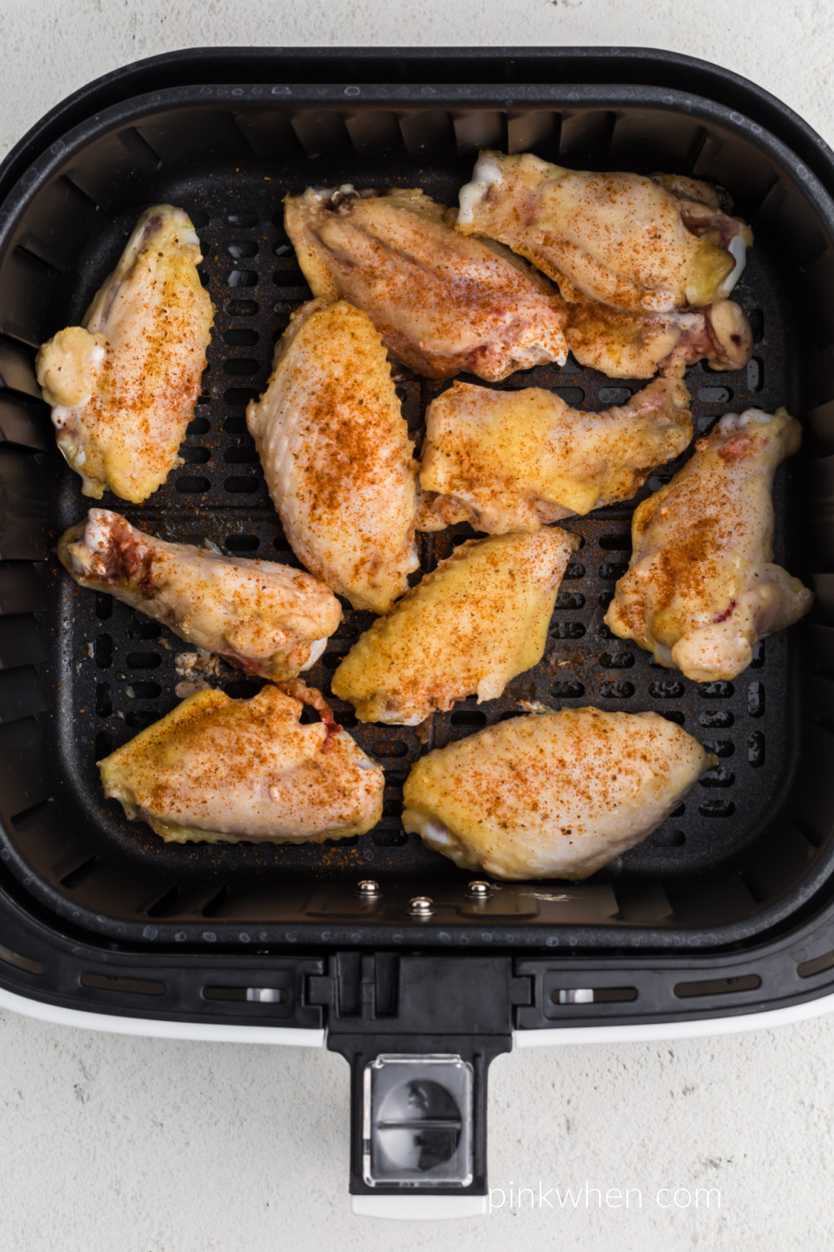 Seasoned wings in the basket of the air fryer, ready to be cooked longer. 