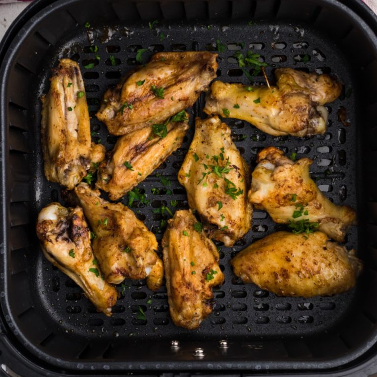 fully cooked chicken wings seasoned and garnished with fresh parsley in the basket of the air fryer.
