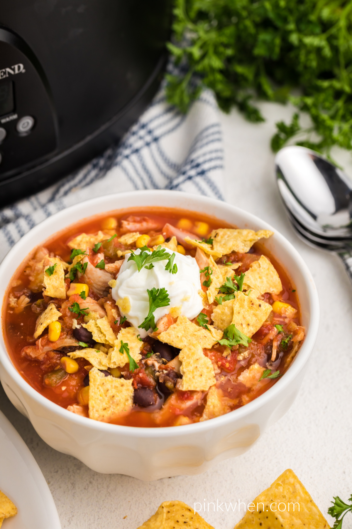Southwestern Slow Cooker Chicken Tortilla Soup in a bowl with crushed tortilla chips, sour cream, and fresh cilantro. 
