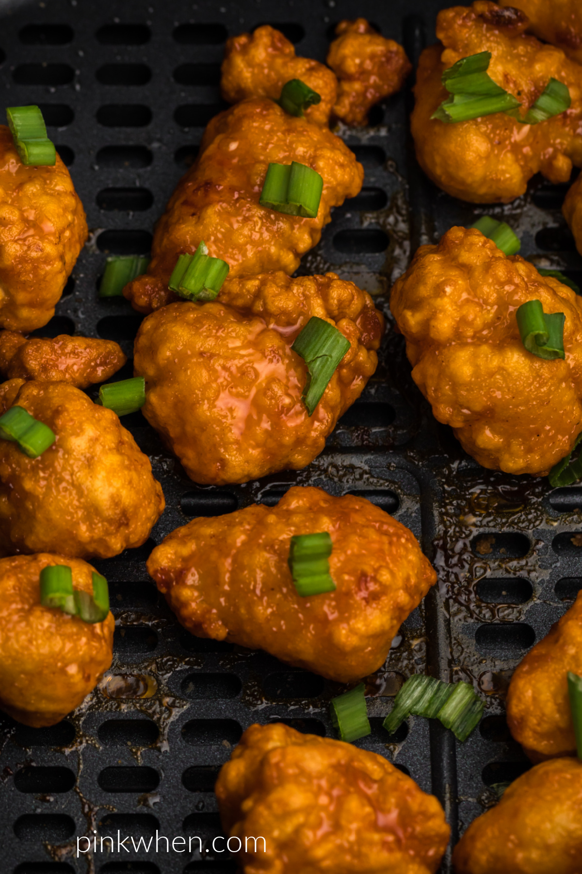 Fully cooked frozen orange chicken in the basket of the air fryer, topped with green onion tops. 