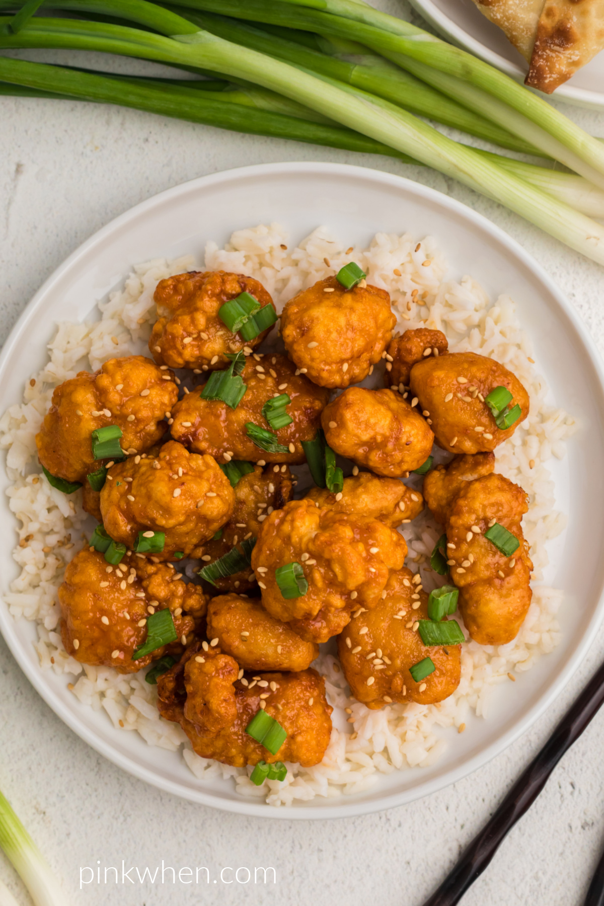 Overhead shot of orange chicken topped with toasted sesame seeds and green onion tops and served over rice. 