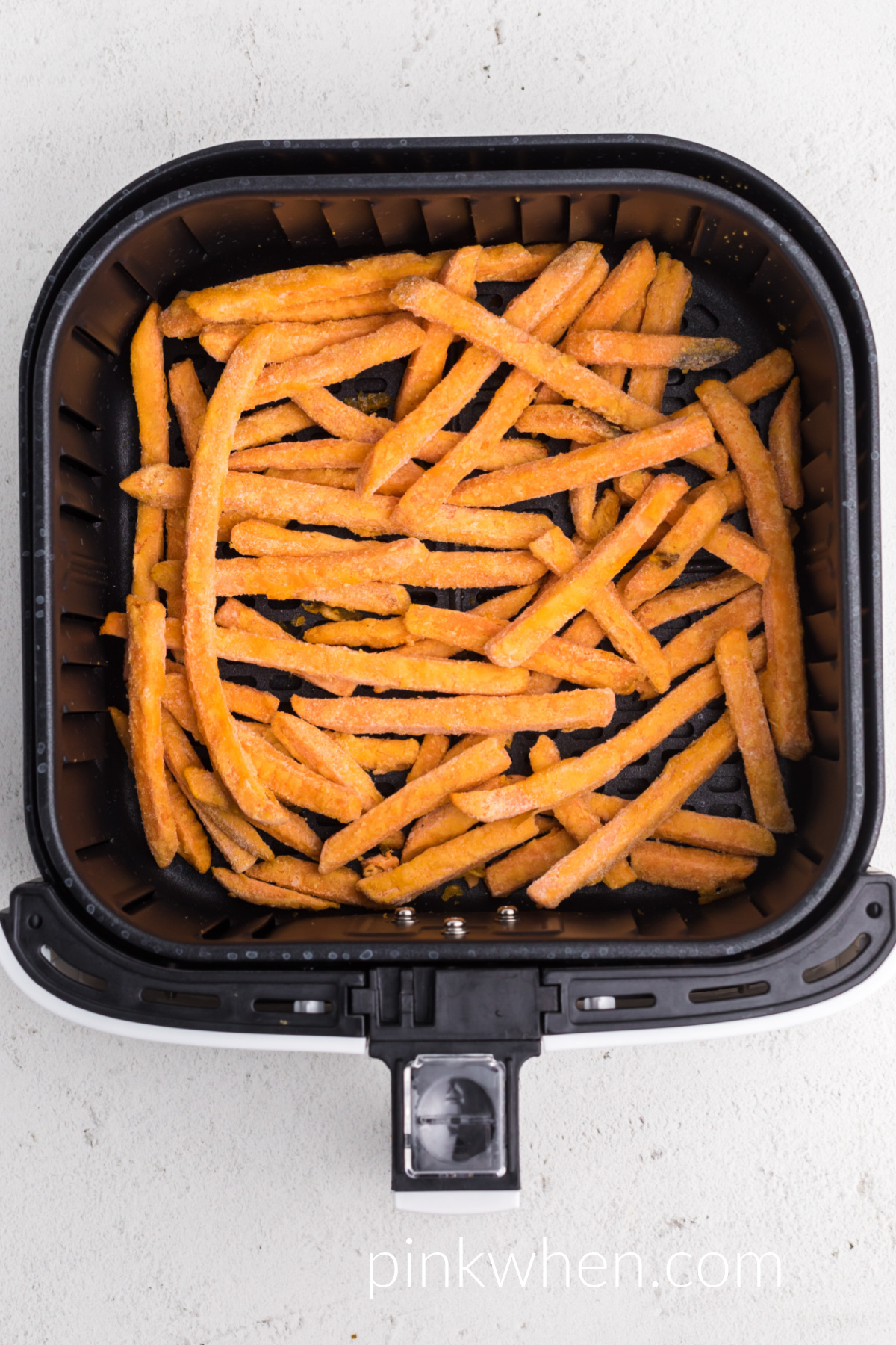 Uncooked frozen sweet potato fries in the basket of the air fryer. 