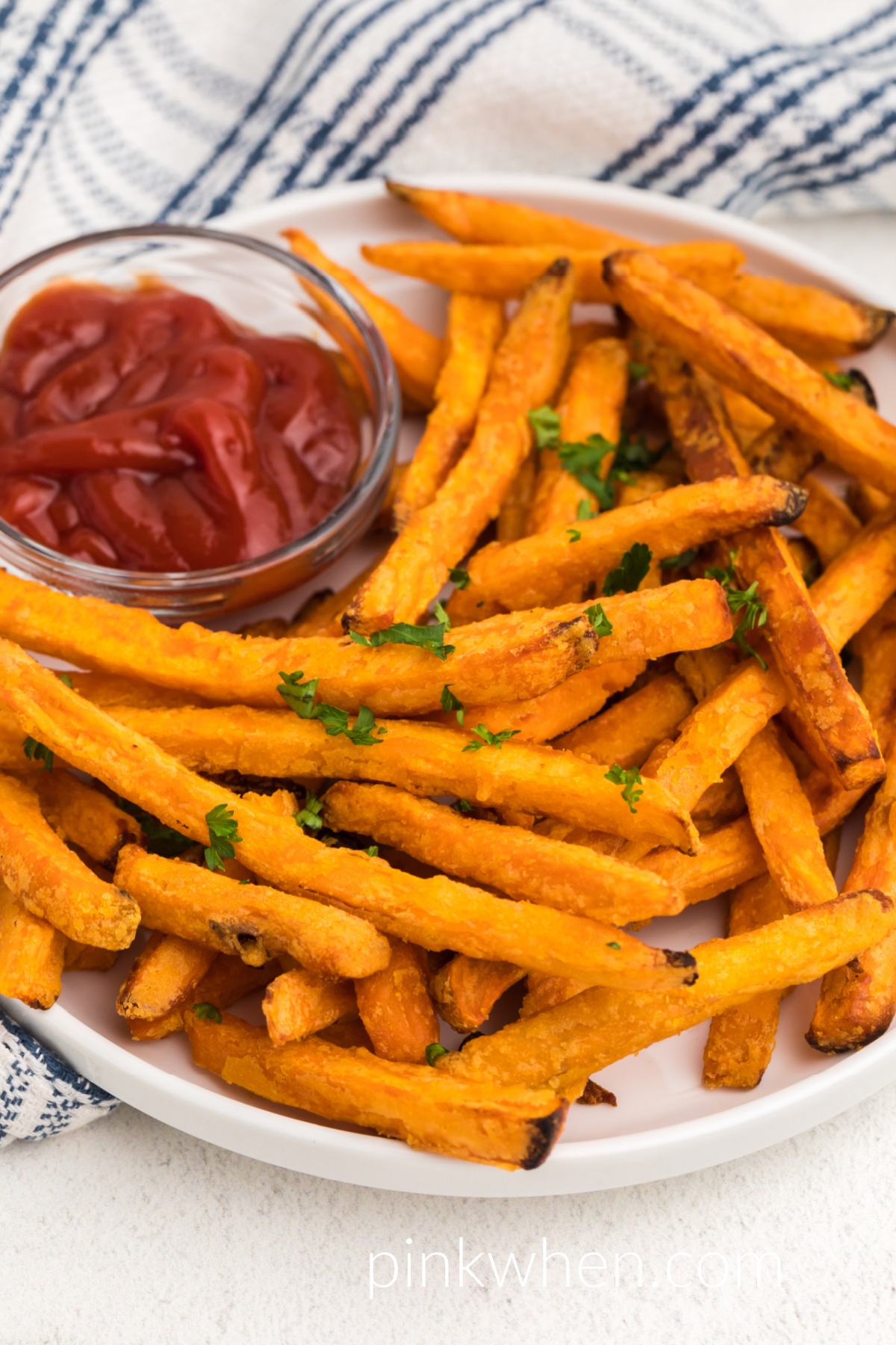 Plate of cooked sweet potato fries made in the air fryer and topped with fresh parsley and served with a side of ketchup. 