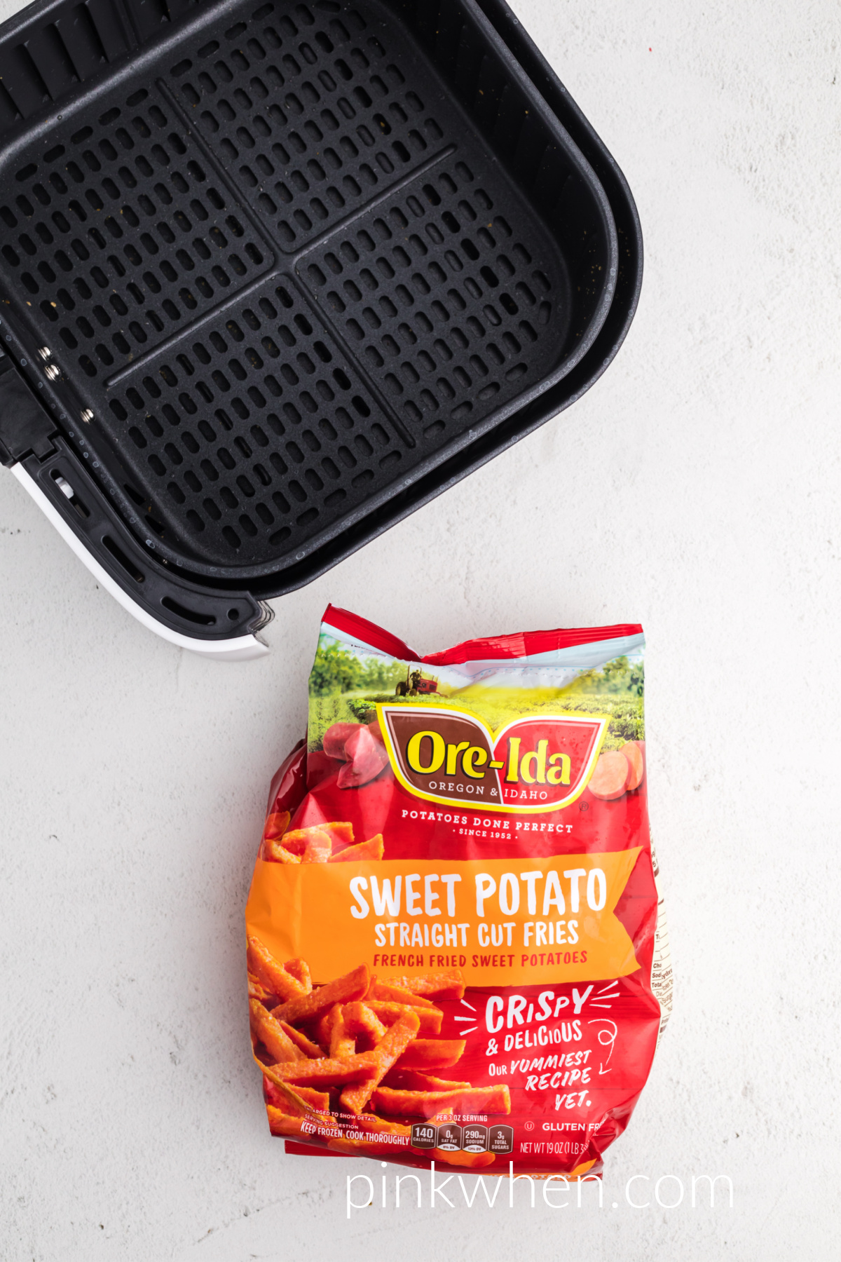 Bag of frozen sweet potato fries and an air fryer basket on a white table. 