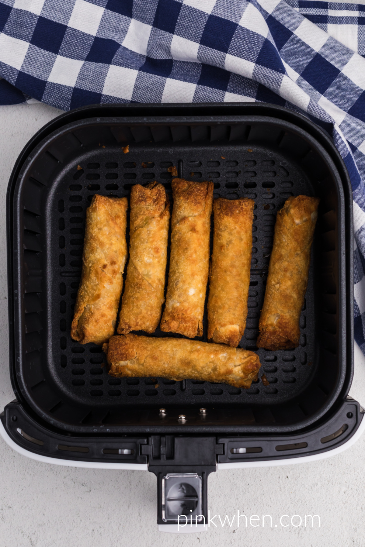 cooked frozen egg rolls in air fryer basket. 