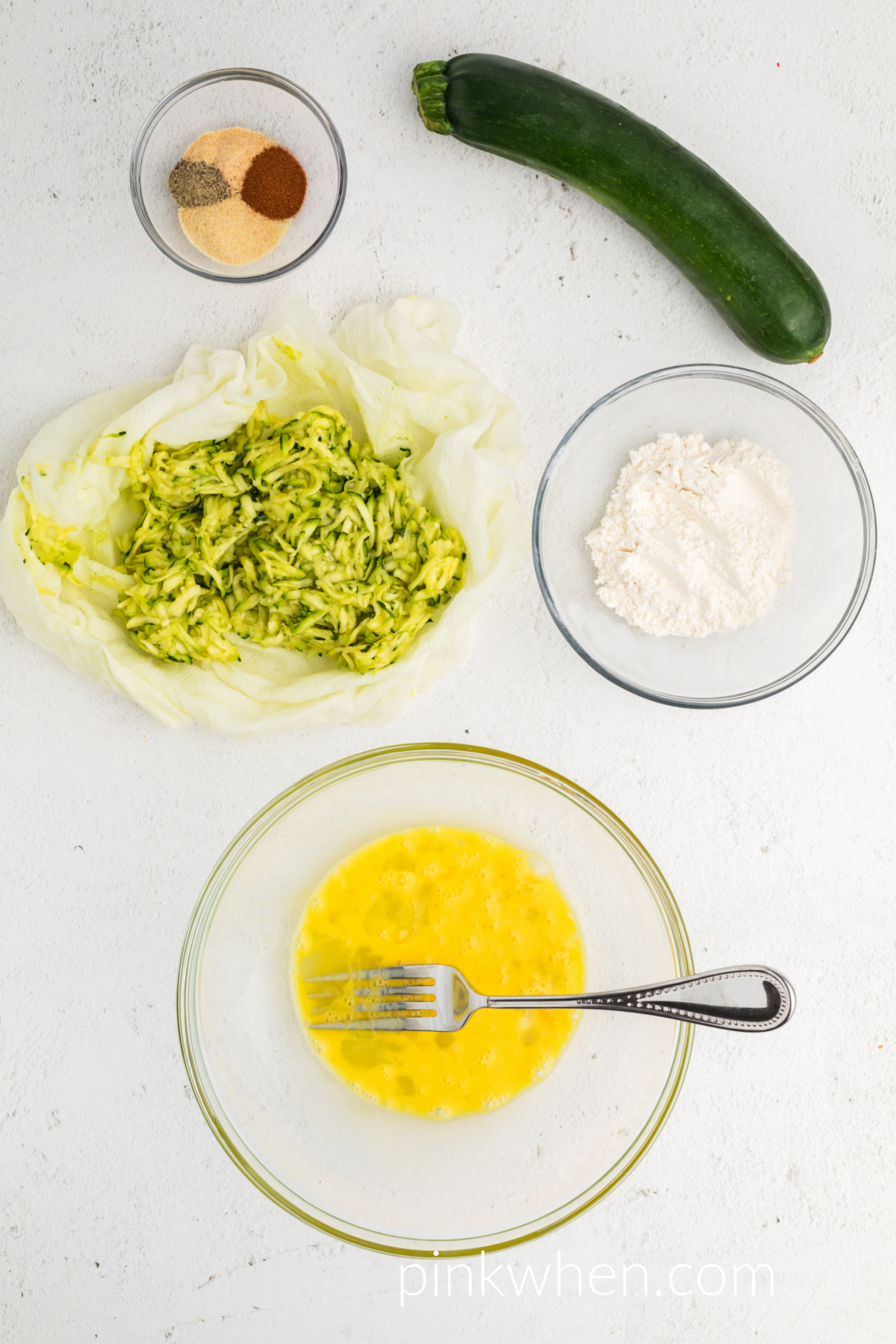 Egg whisked together in a bowl and ingredients needed to make zucchini fritters in the air fryer.