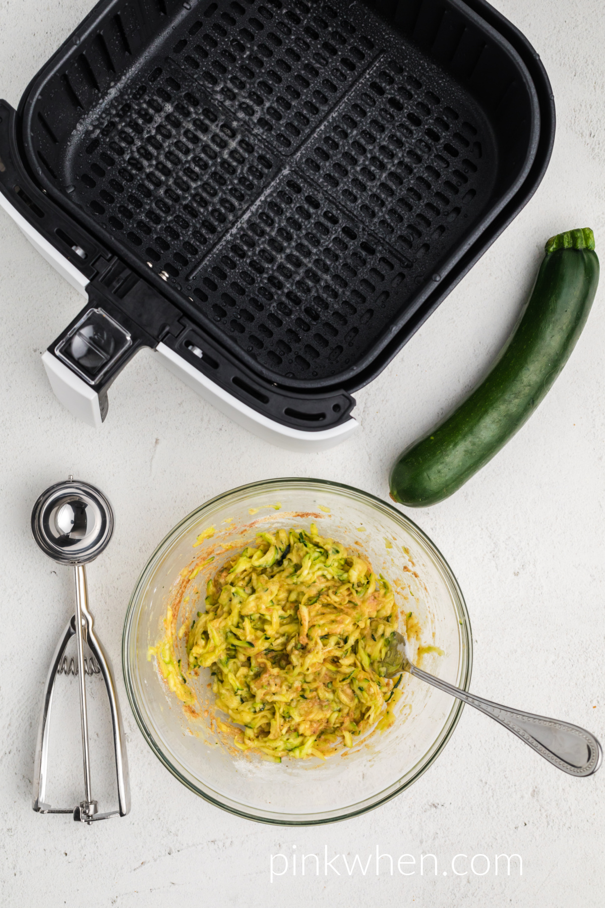 shredded zucchini and ingredients needed to make fritters mixed together in a bowl. 