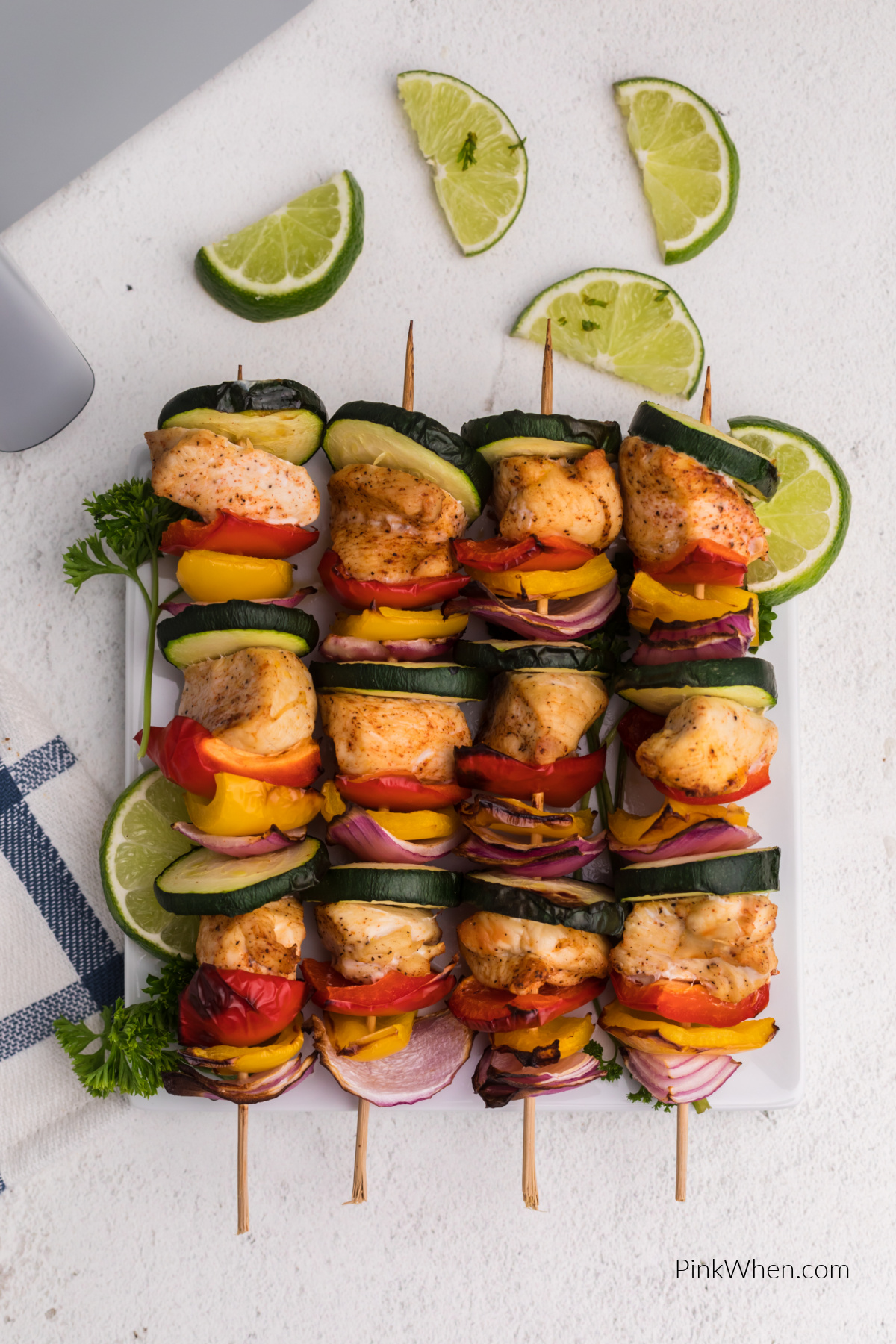 Overhead photo of chicken kabobs on a white plate with sliced limes. 
