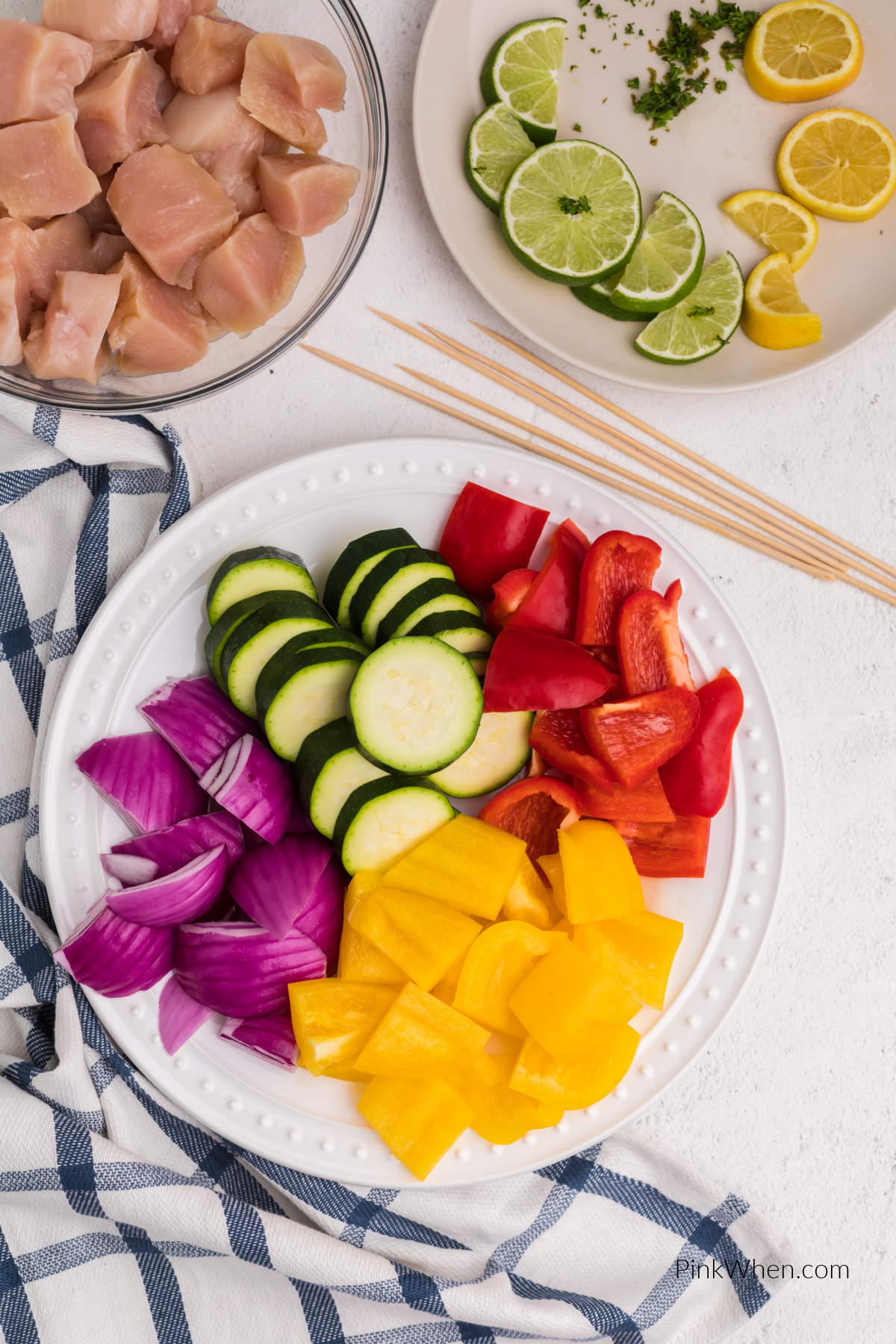 Plate full of cut onion, bell peppers, and zucchini, sliced lemon and peppers, and a bowl of cut chicken.