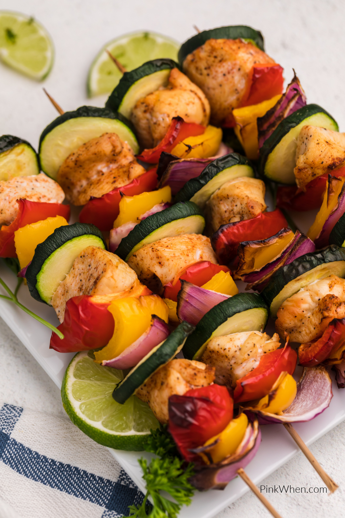 Chicken kabobs made in air fryer and served on a white plate with slices of lime.
