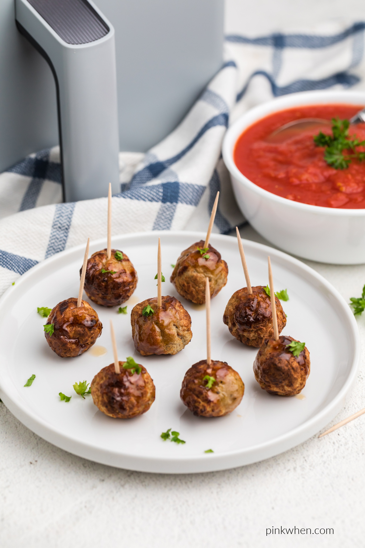 Meatballs on a white plate topped with fresh parsley and served with toothpicks.