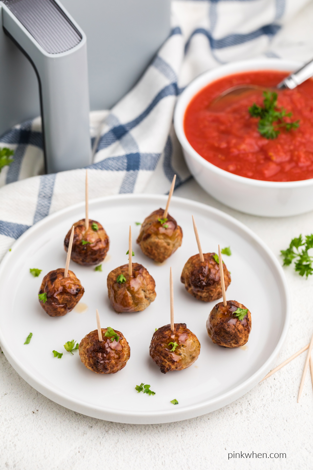 Air fried meatballs from frozen served on a white plate with toothpicks and fresh parsley.