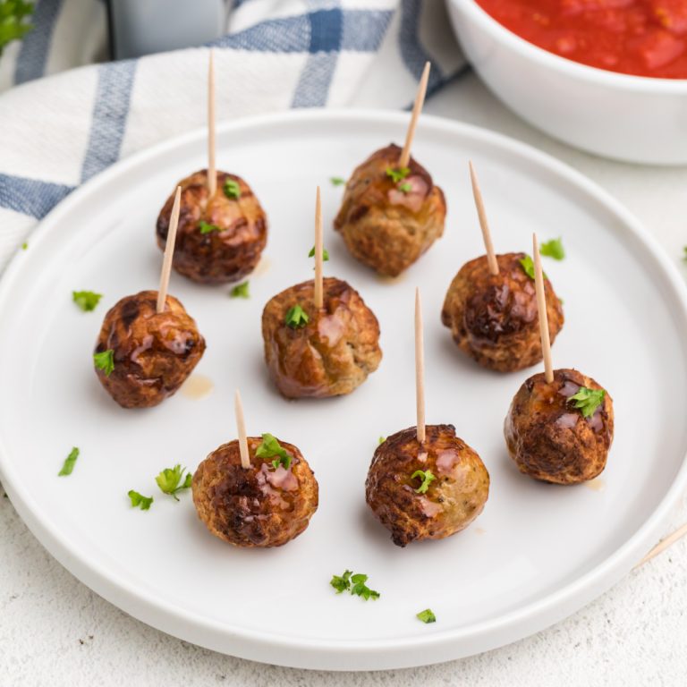 CLose up of air fried meatballs made from frozen and served on a plate with toothpicks and topped with fresh chopped parsley.