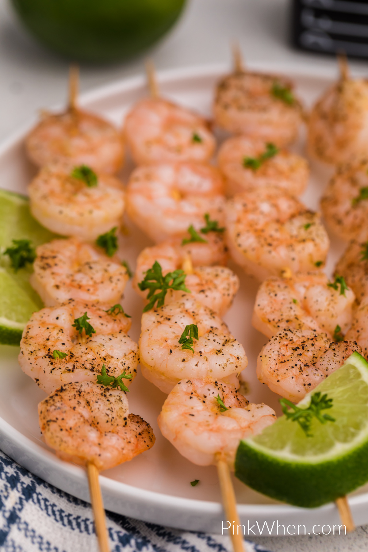 Shrimp skewers on a white plate with slices of lime. 