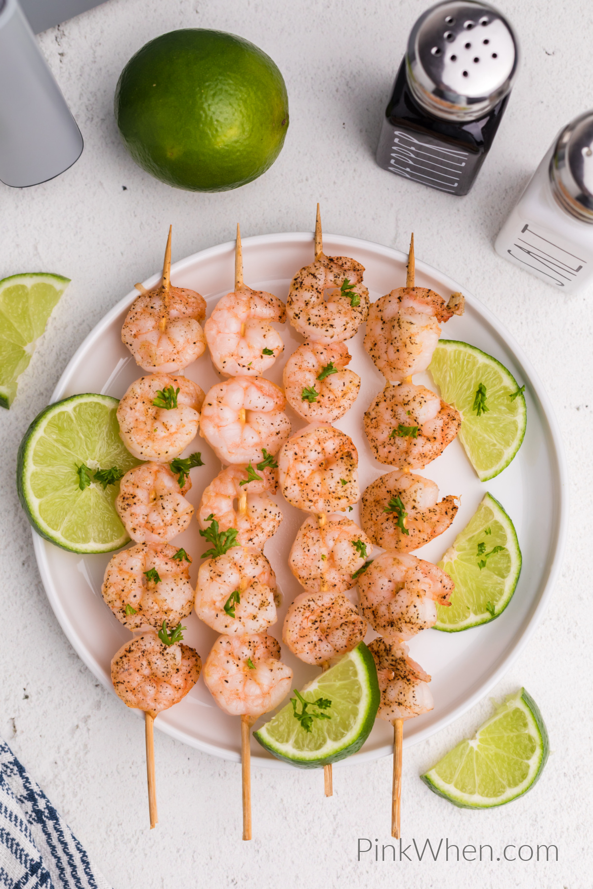 Overhead photo of shrimp skewers on a white plate with slices of lime, ready to eat. 