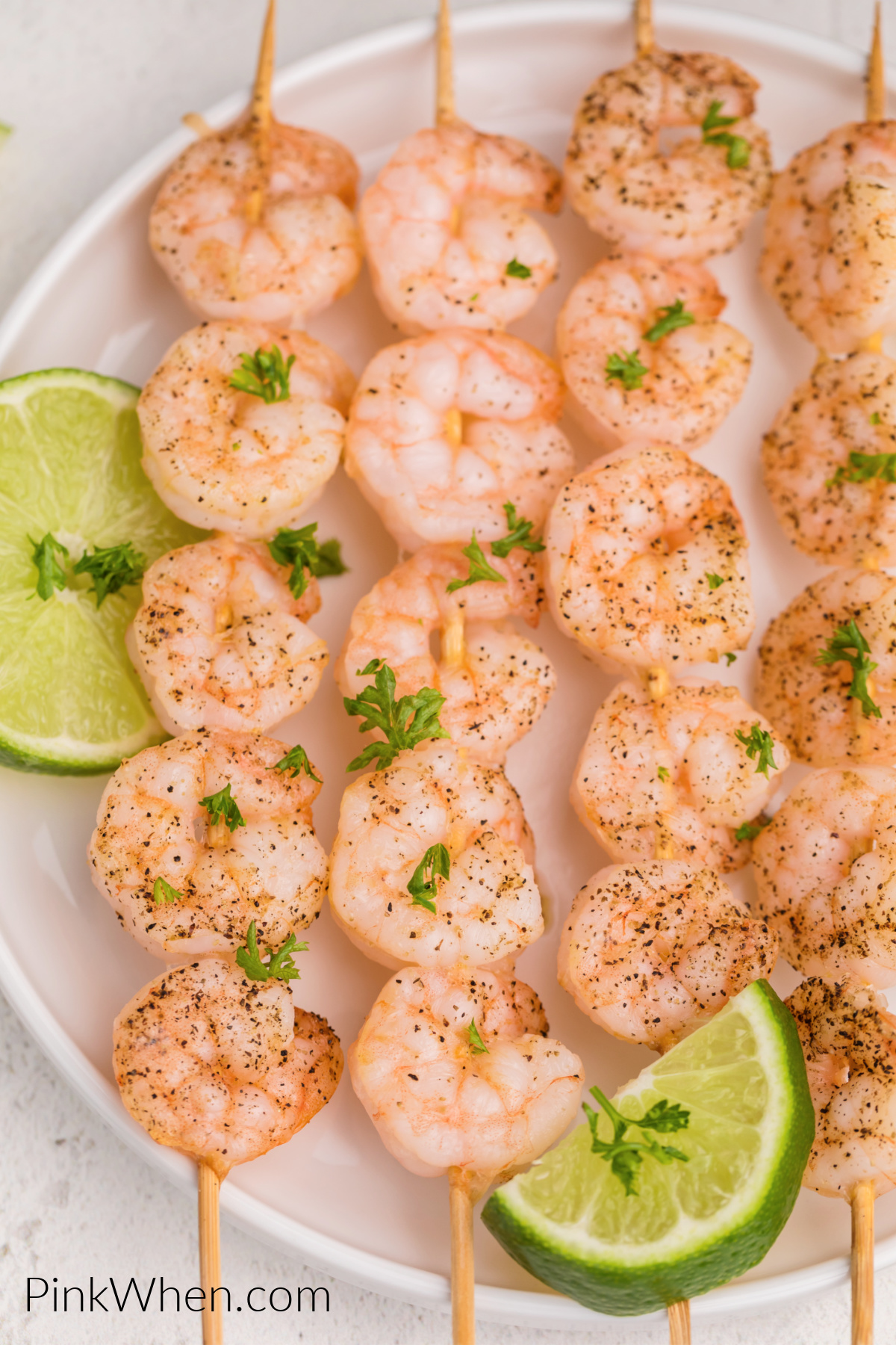 Shrimp skewers made in the air fryer and served on a white plate with sliced of lime.
