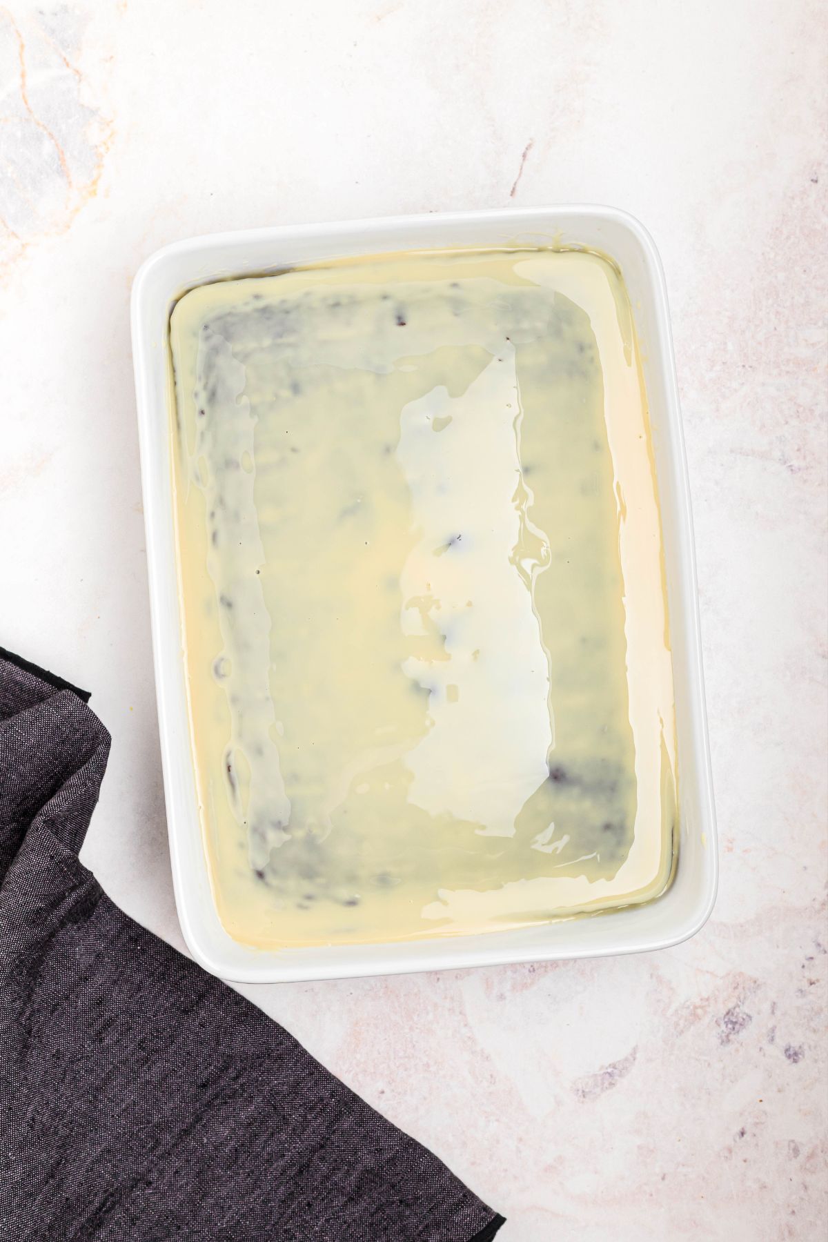 Baked cake in a white rectangle baking dish, with sweetened condensed milk poured over the top.