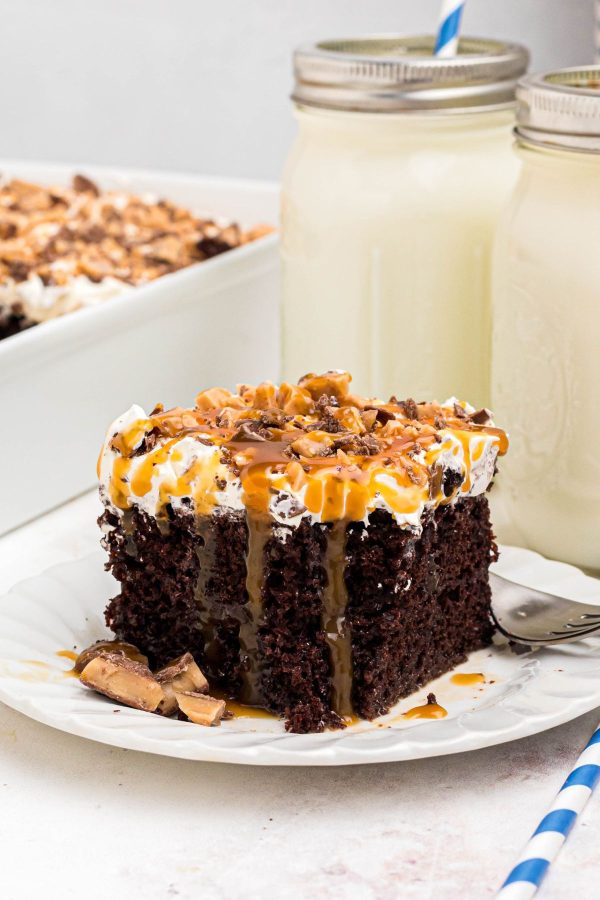 Rich chocolate slice of cake with whipped cream topping and drizzles of caramel sauce, on a white plate. 
