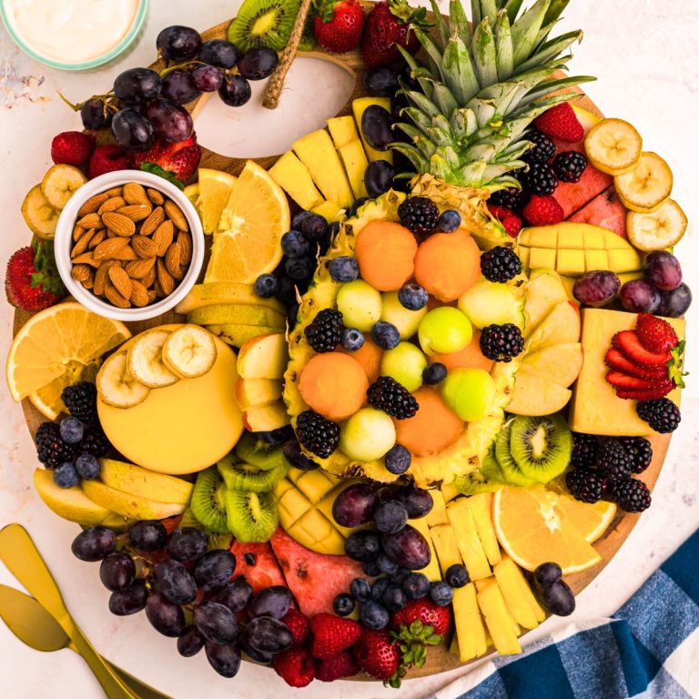 Various fruits cut and sliced filling a round charcuterie board.