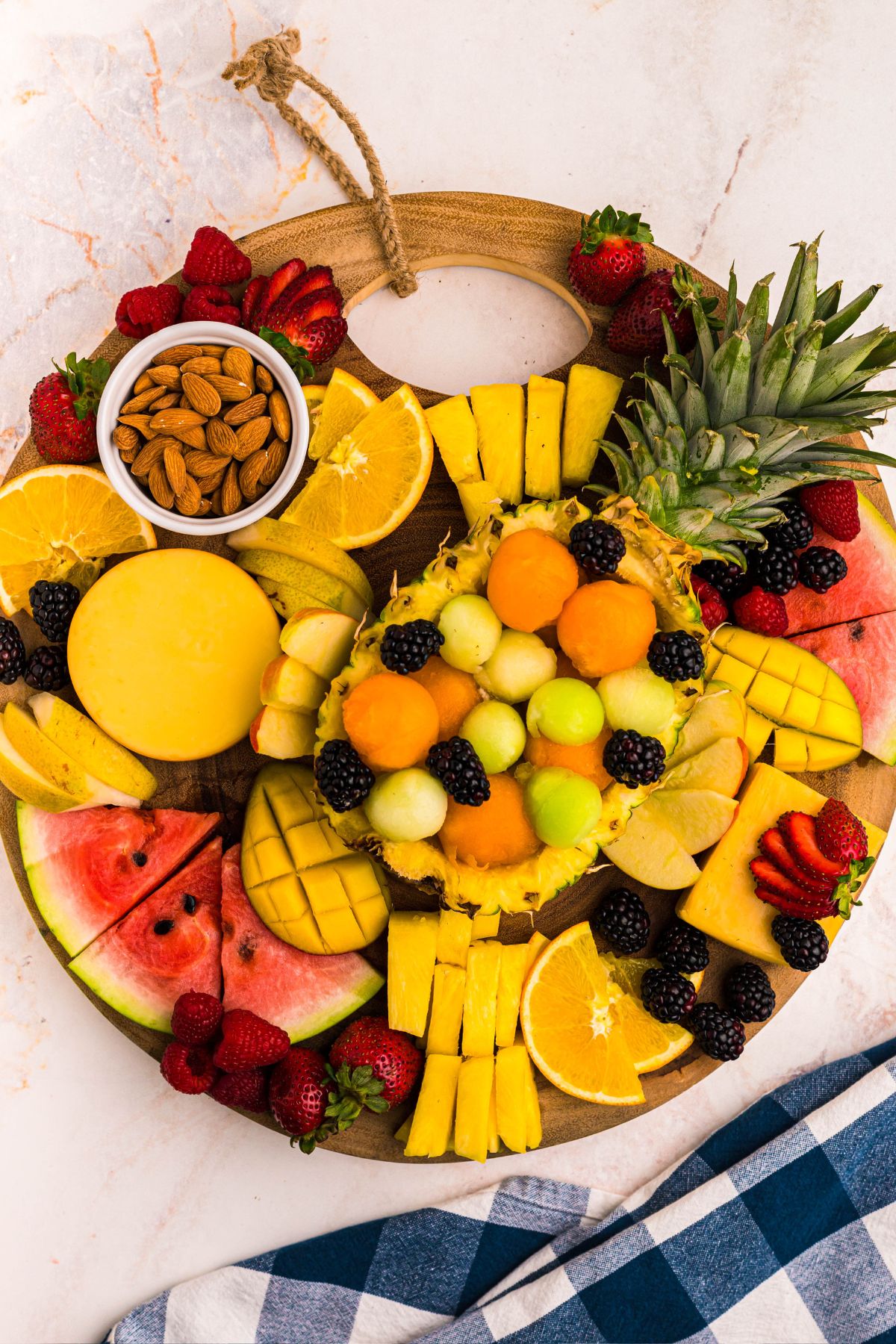 Slices of fruits and berries being added to a round wooden charcuterie board. 