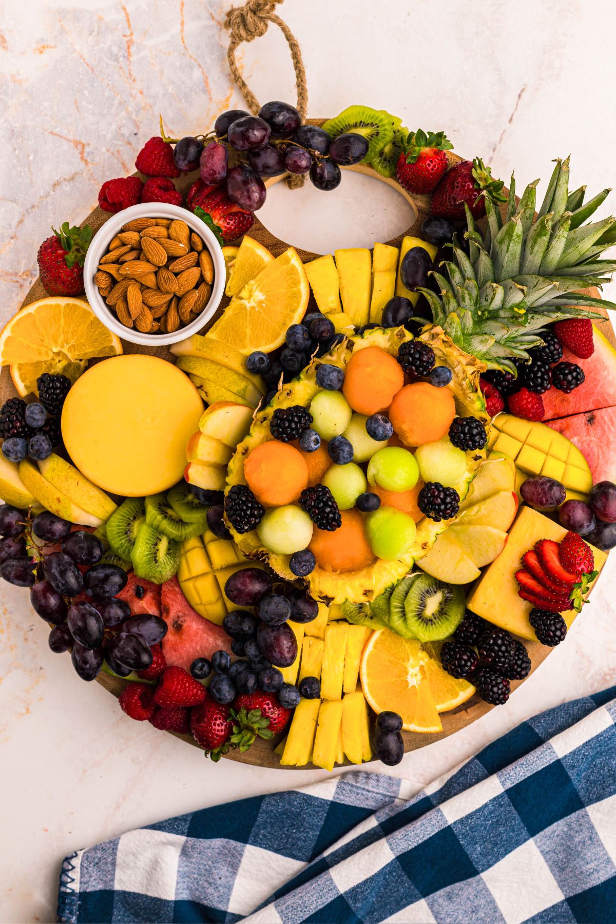 Various fruits scattered on a round charcuterie board with grapes and nuts filling empty spots