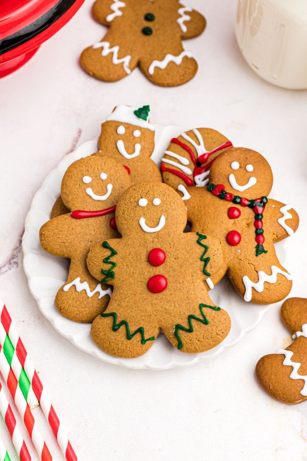 Golden decorated gingerbread cookies on a white plate in front of milk