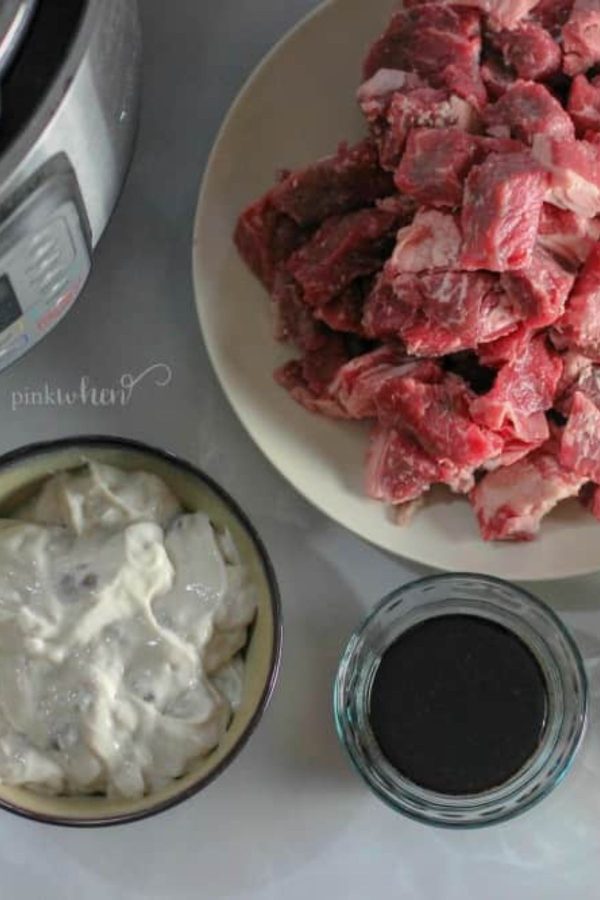 Uncooked beef tips, cream of mushroom soup, sauce, and instant pot on a white marble table. 