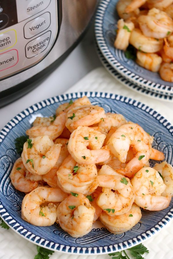 Golden orange cooked shrimp on a blue plate, sprinkled with parsley flakes, in front of an Instant Pot.