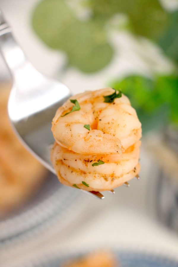Orange shrimp sprinkled with parsley flakes being served on a fork. 