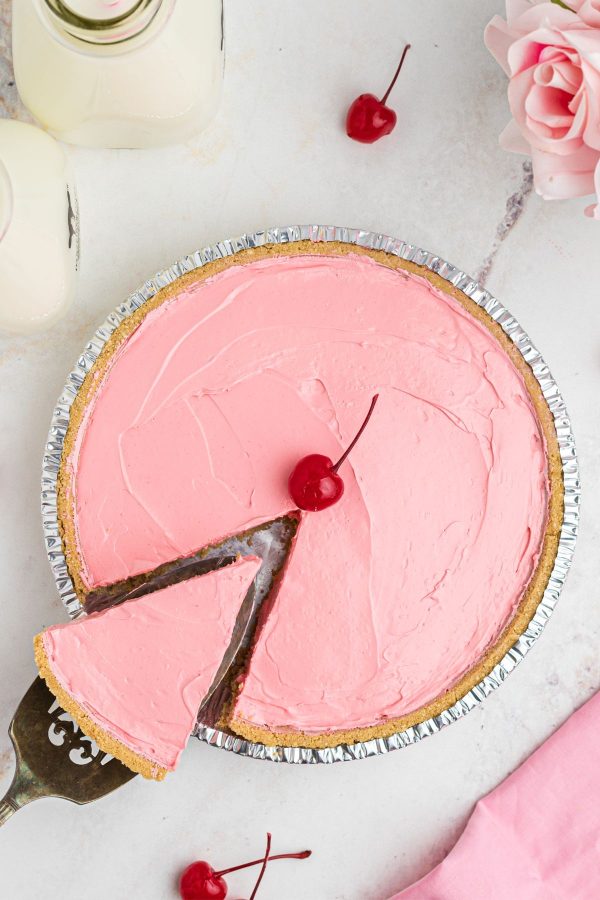 An overhead photo of a pink kool aid pie with a slice being removed with a spatula