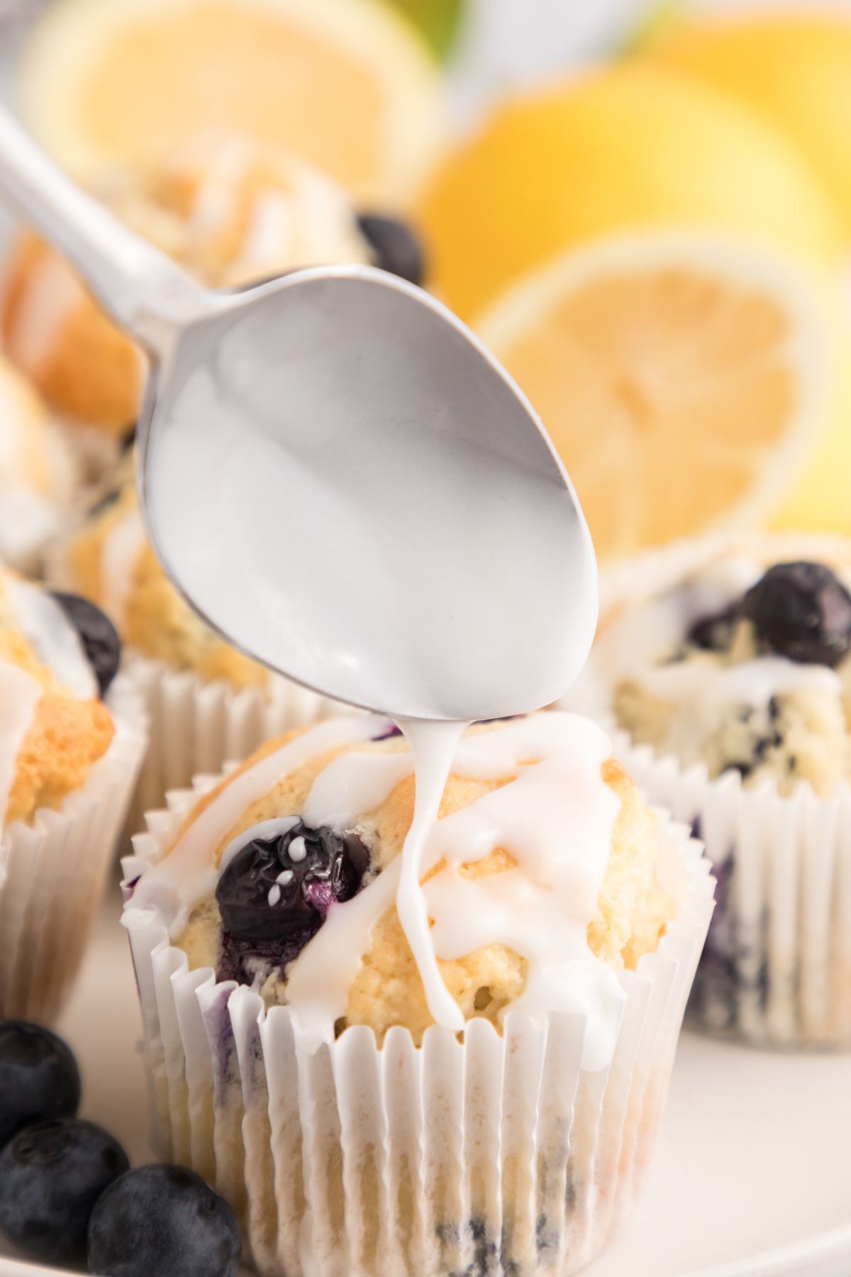 Golden baked muffins being drizzled with lemon glaze on top.