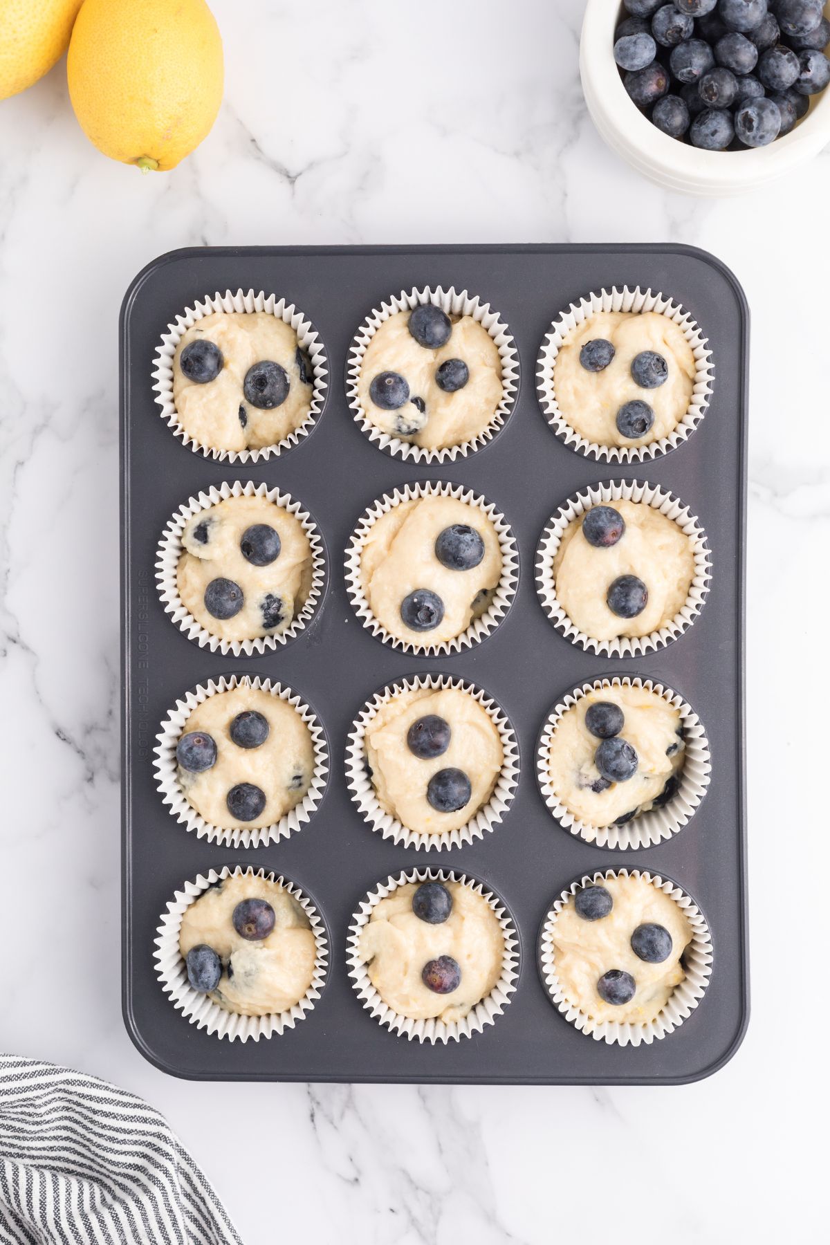 Muffin batter in muffin tin on a white marble table