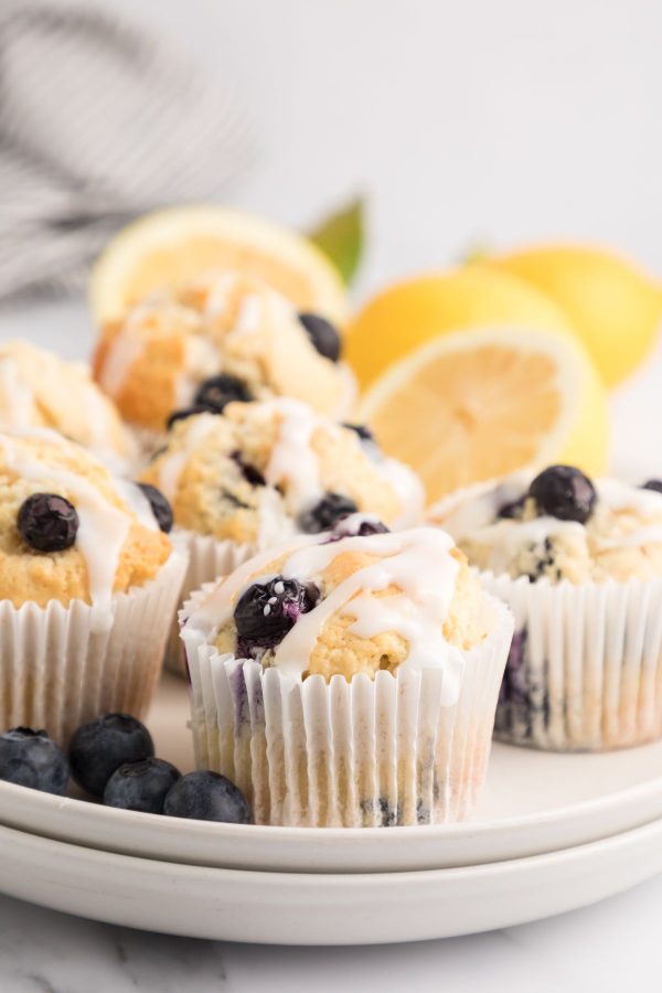 Golden baked lemon blueberry muffins on a white plate with fresh blueberries and lemons